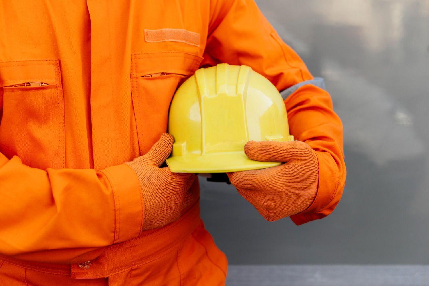 A man in an orange jumpsuit is holding a yellow hard hat.