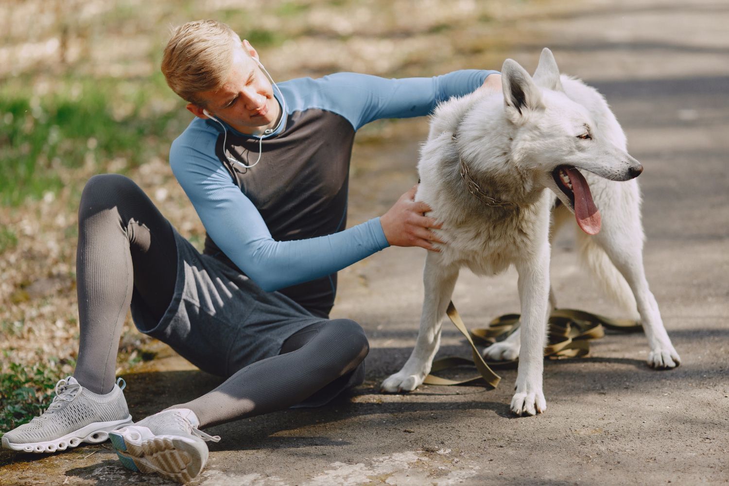 A man is sitting on the ground petting a white dog.