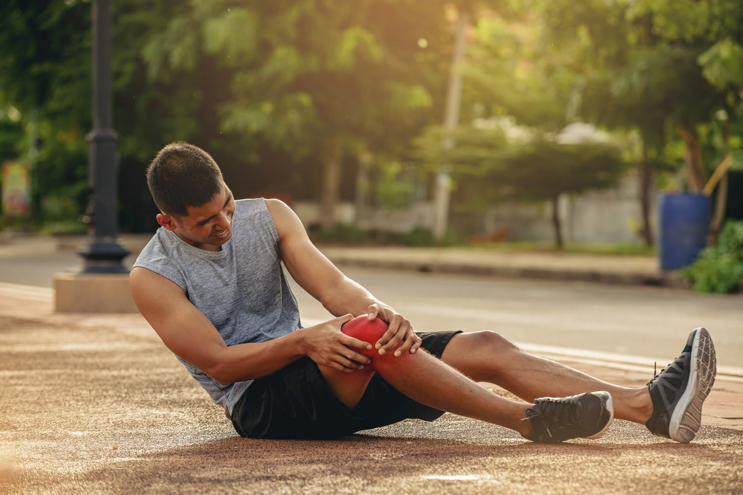 A man is sitting on the ground holding his knee in pain.