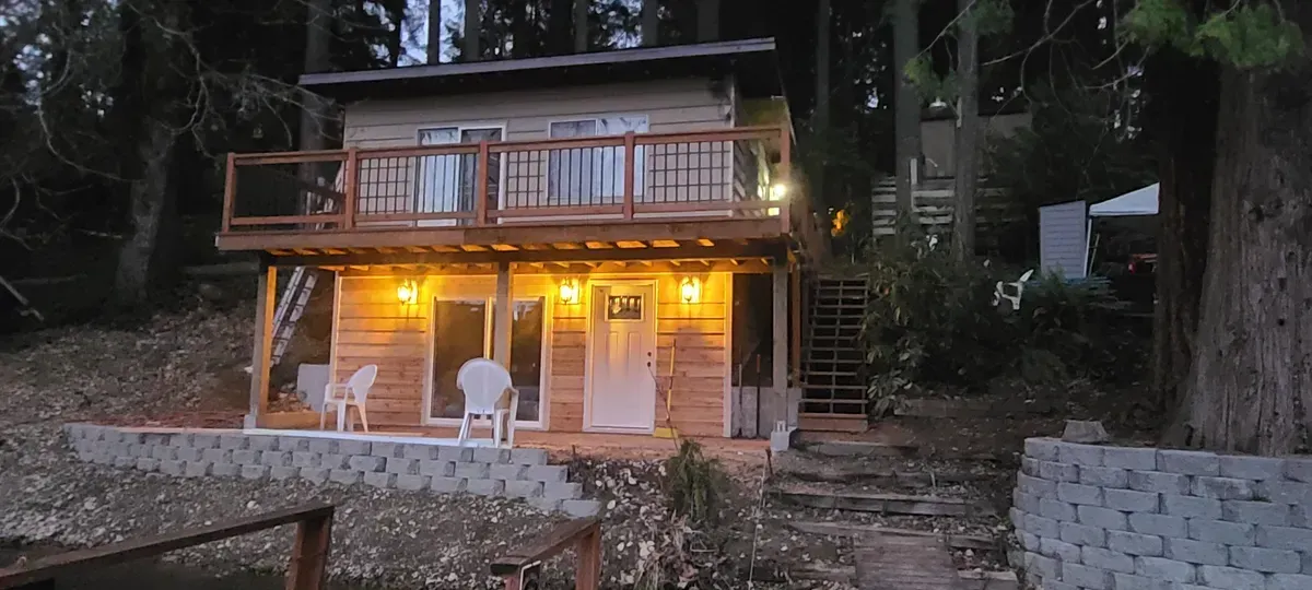 A small wooden house with a large deck in the middle of a forest.