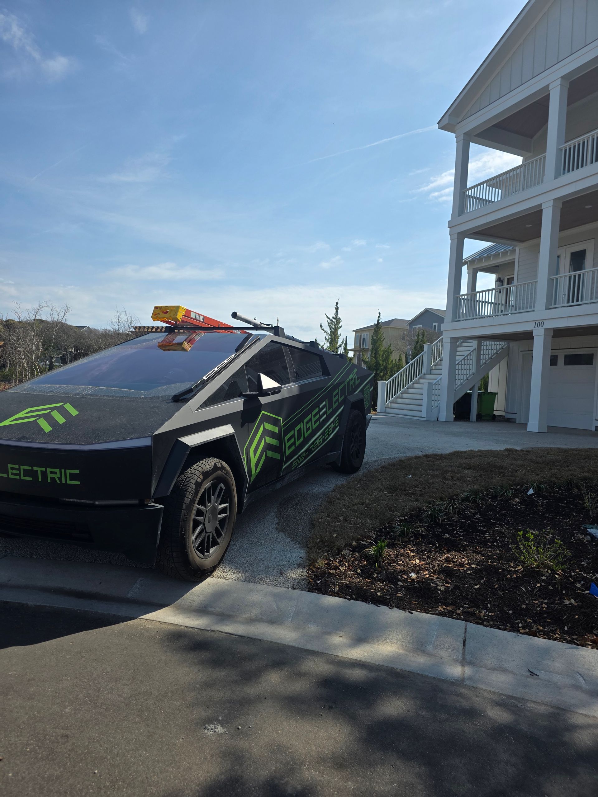 Black electric sports car parked beside a white building under a bright blue sky.
