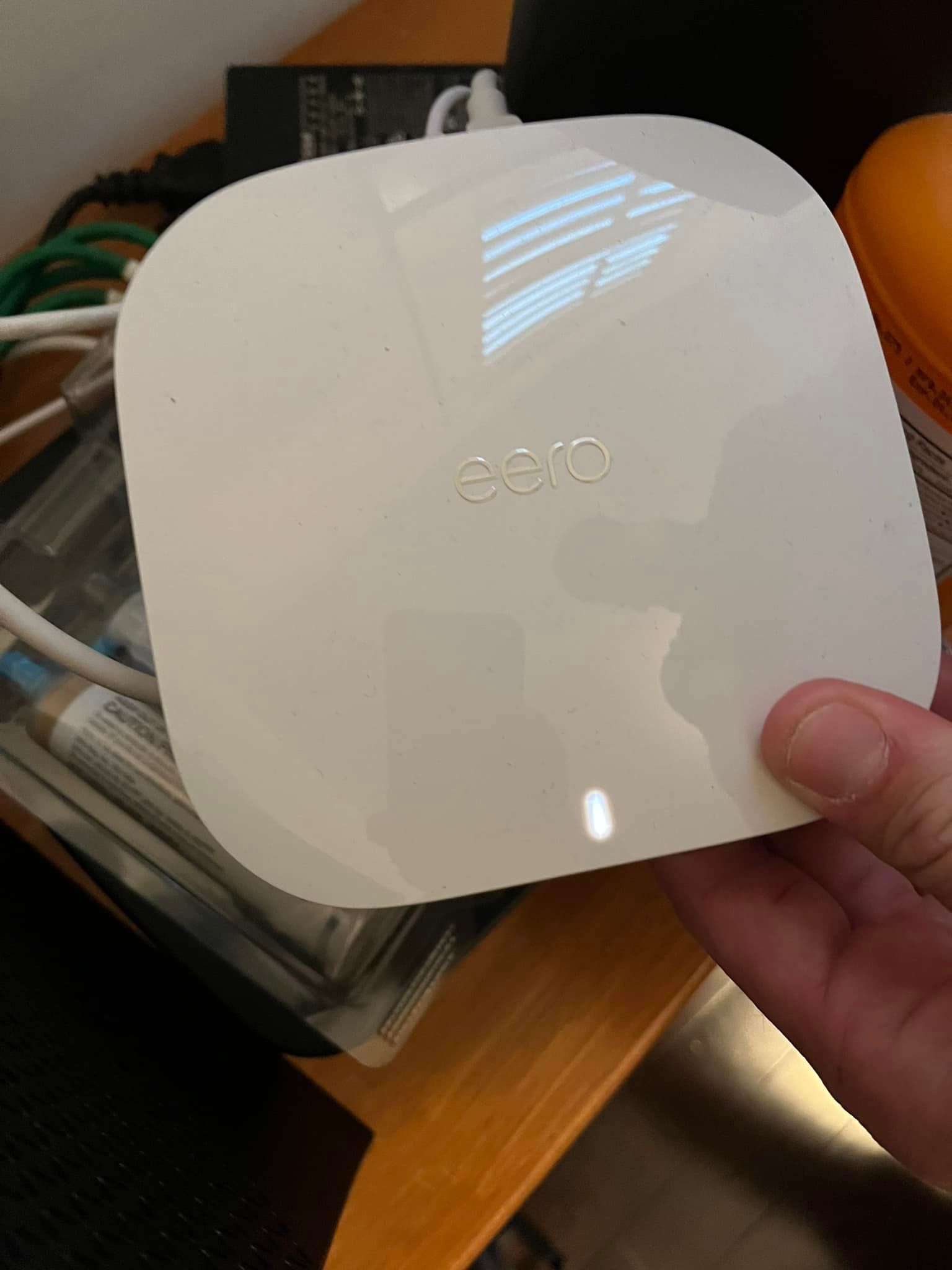 White wireless access point held by a hand; illuminated status light.