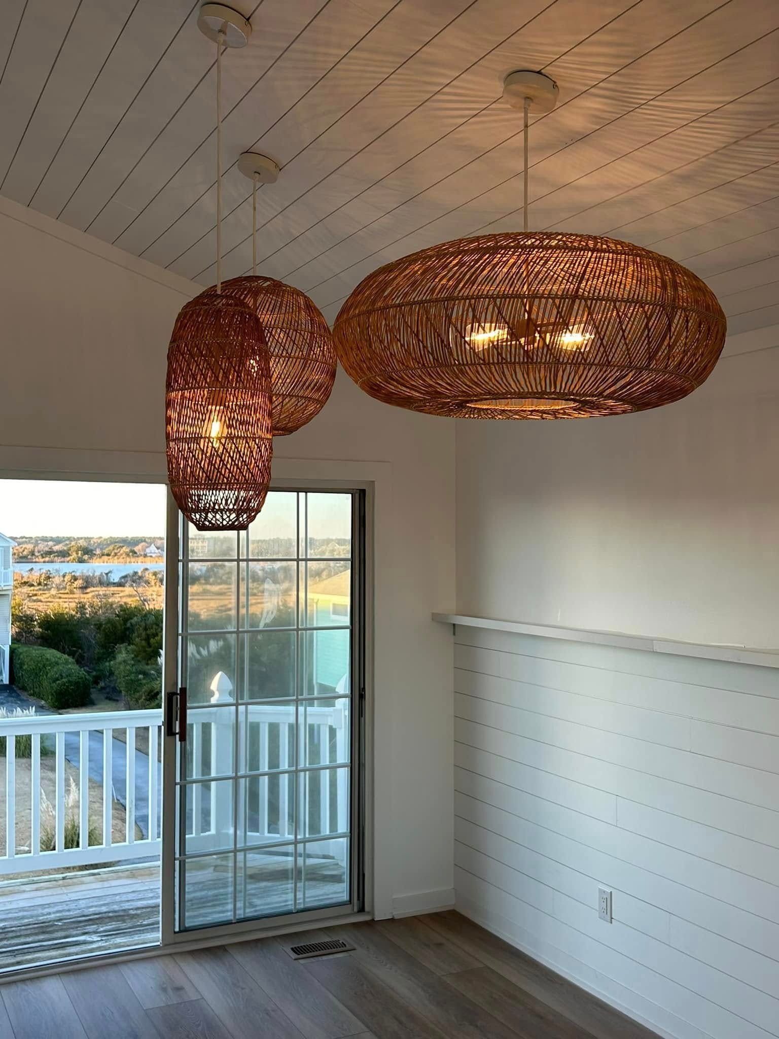 Three woven pendant lights over a dining area with a view through glass doors.