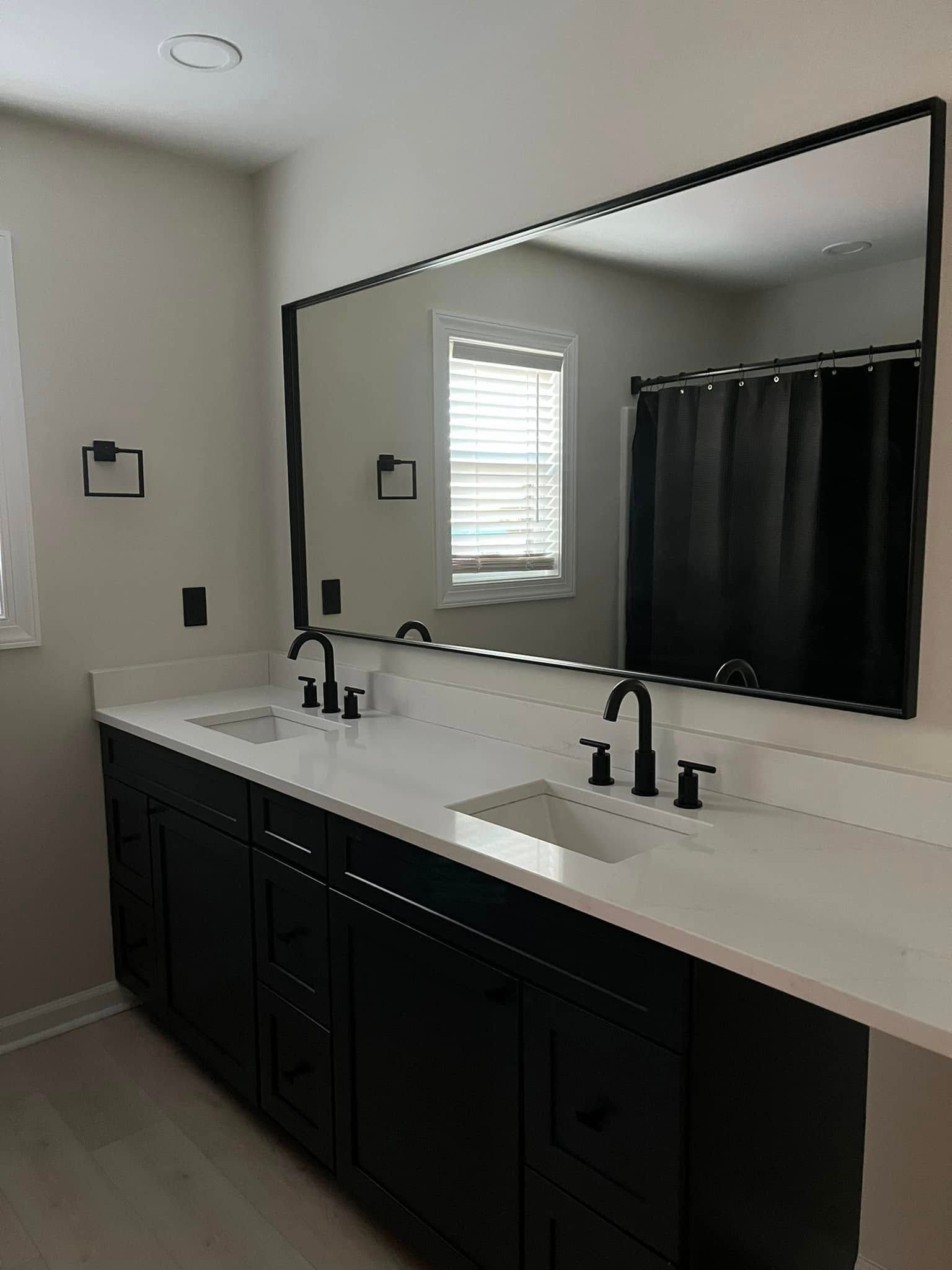 Black double vanity in a bathroom with a large mirror and white countertop.