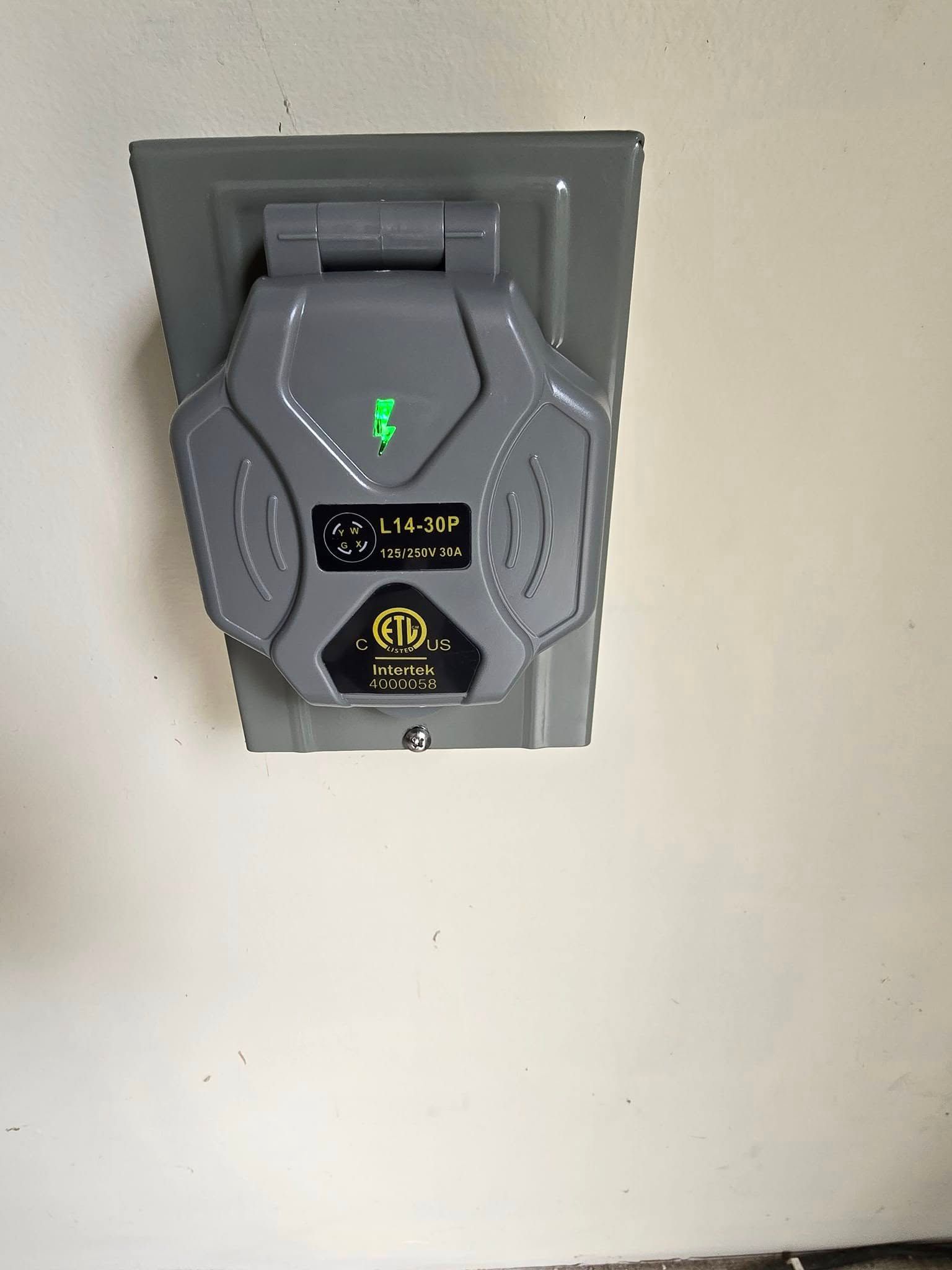 Gray electric vehicle charger mounted on a wall; green light illuminated.