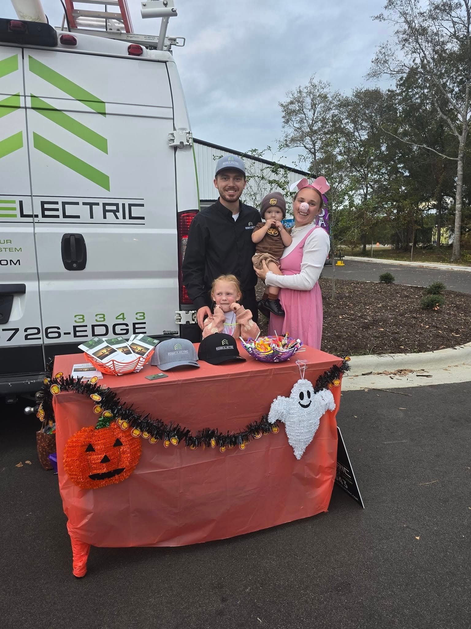 Family poses in front of a van with a Halloween-decorated table.