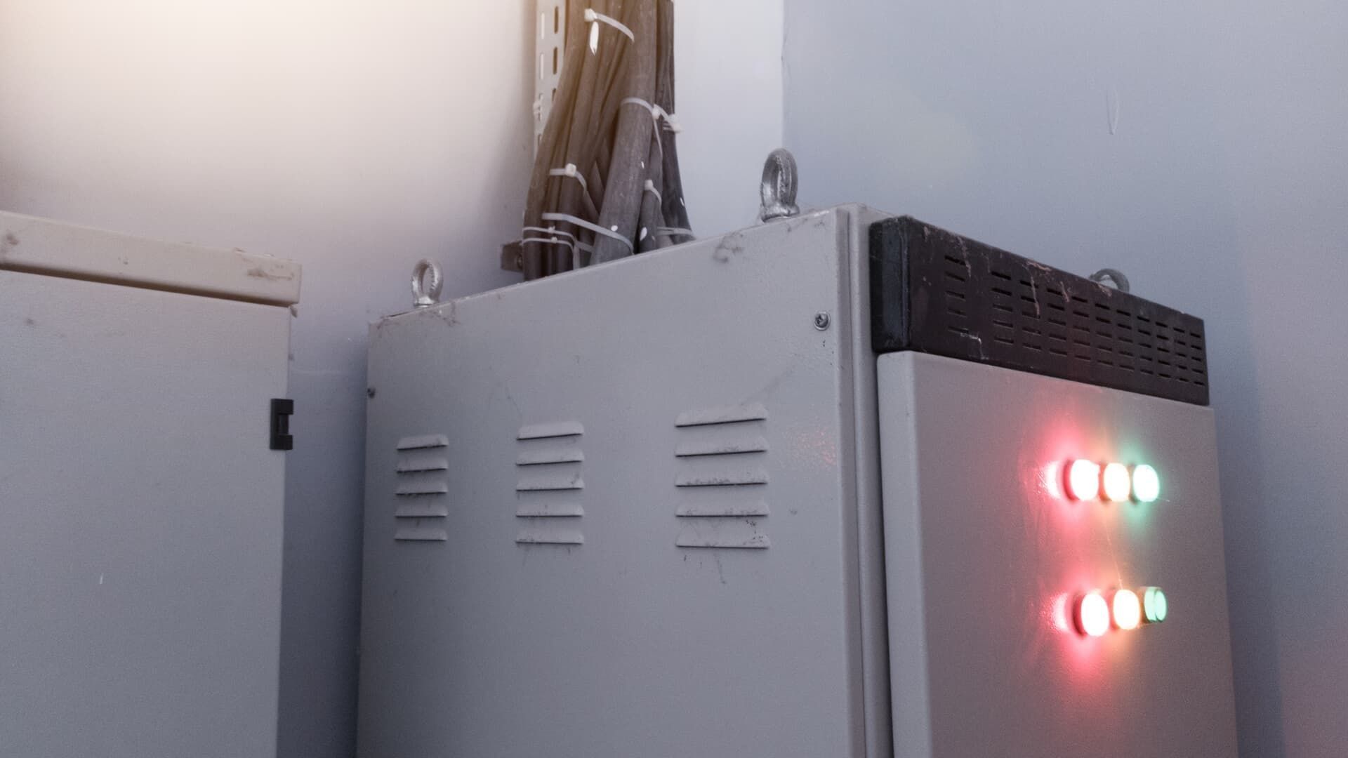 Metal electrical panel with ventilation slots and indicator lights, cables running from top.