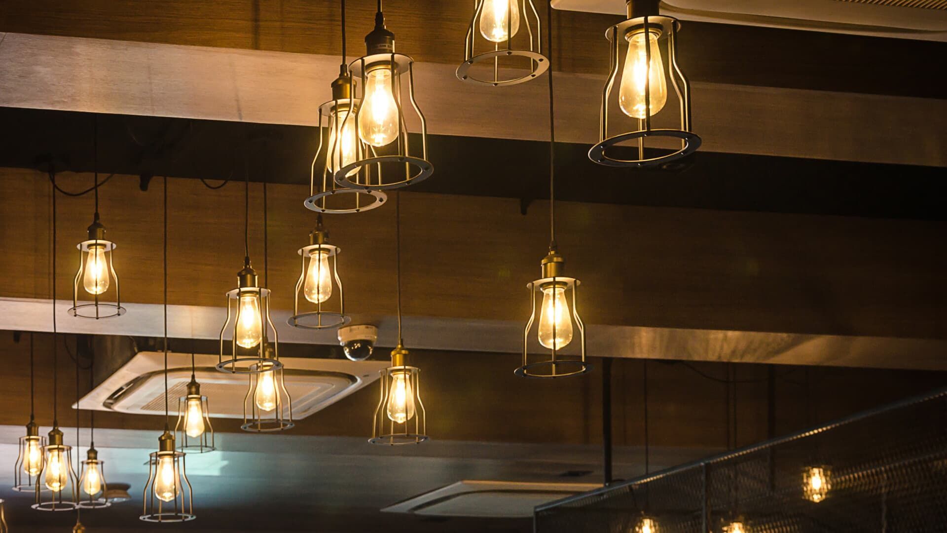 Industrial-style pendant lights with exposed bulbs hanging from a dark ceiling, providing warm illumination.