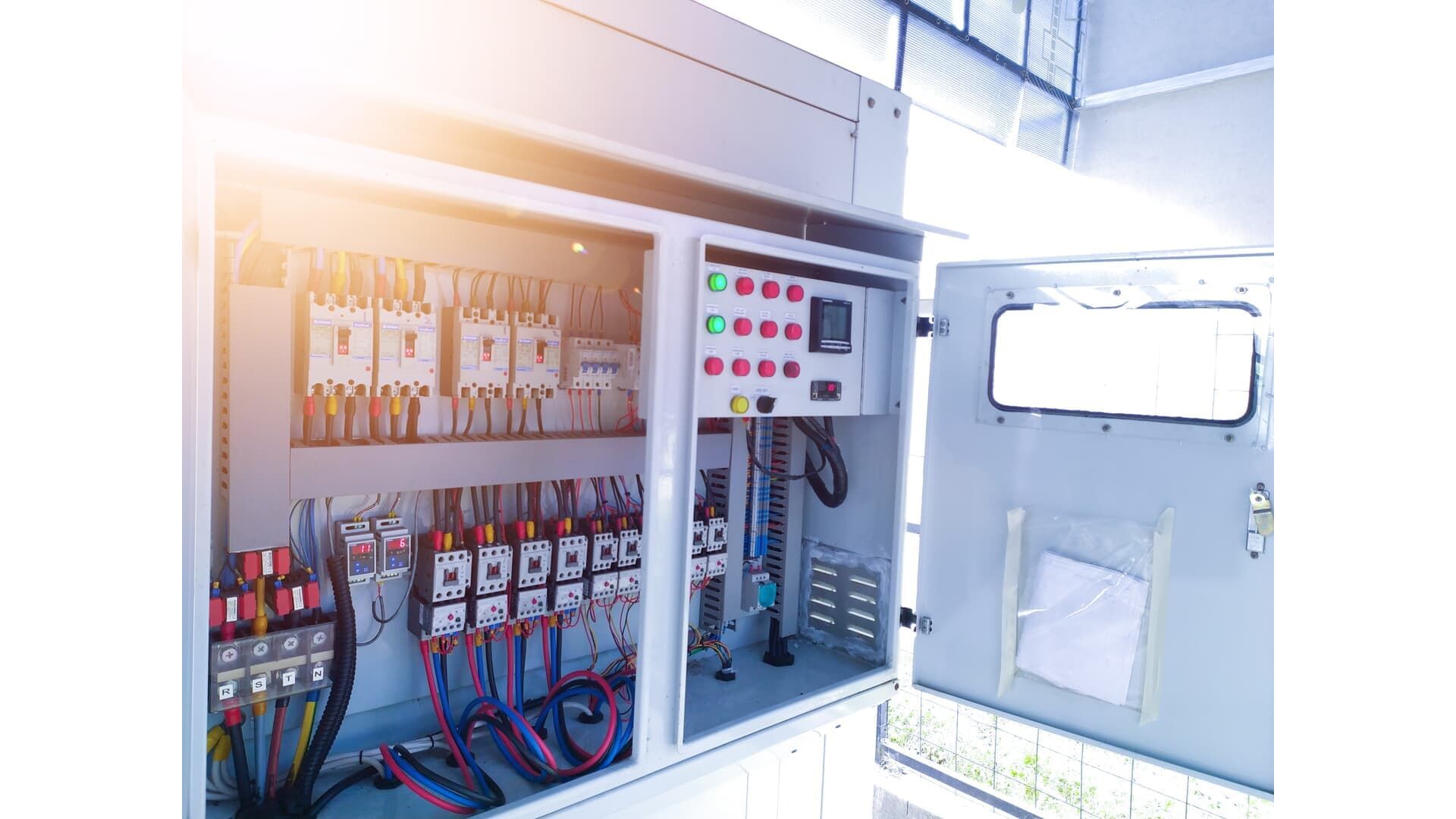 Opened electrical control panel with wires, switches, and meters. Bright interior, outdoor setting.