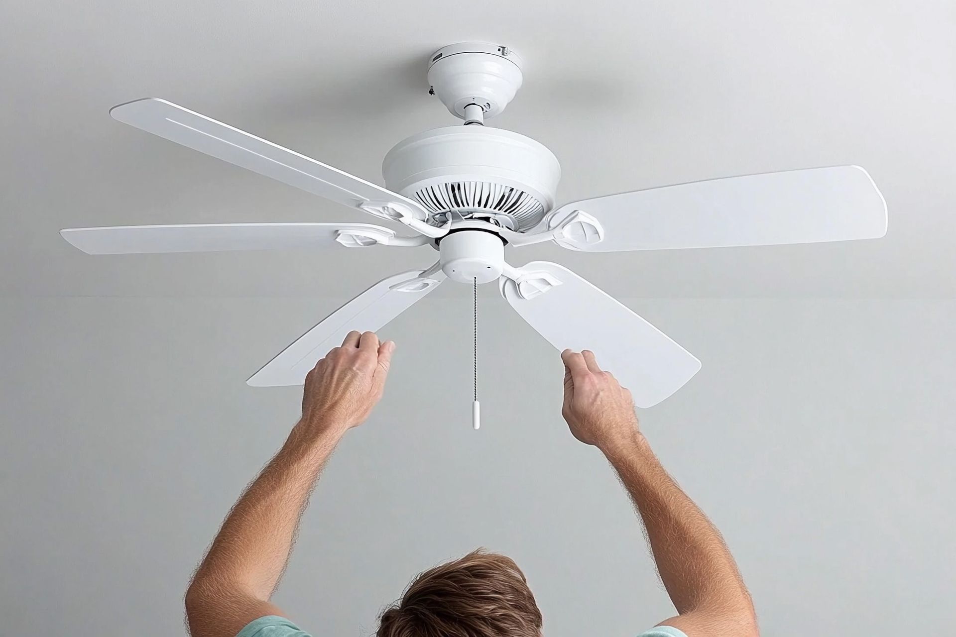 Person installing a white ceiling fan in a room with a light gray ceiling.