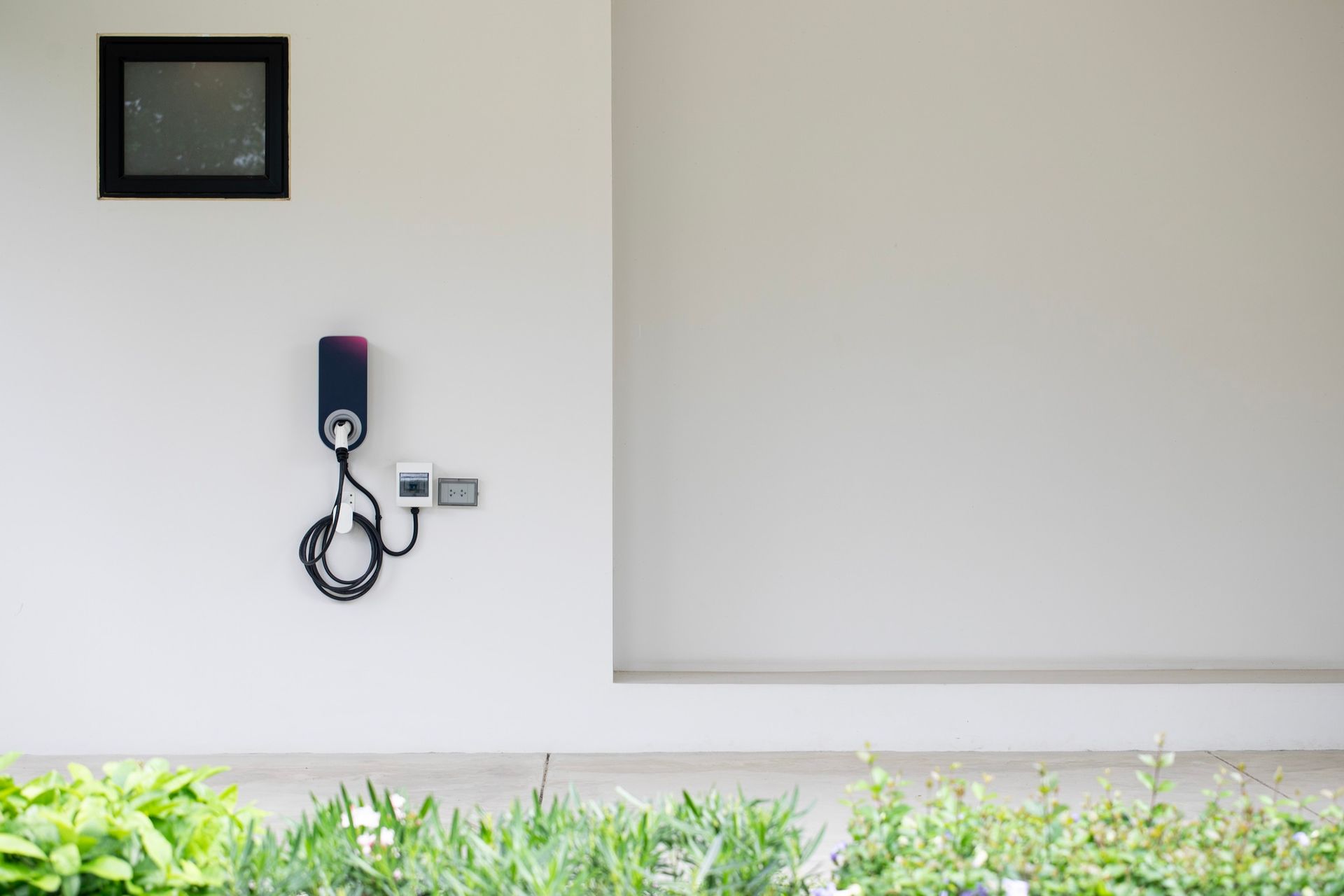 Electric vehicle charger mounted on a white wall with a window above.