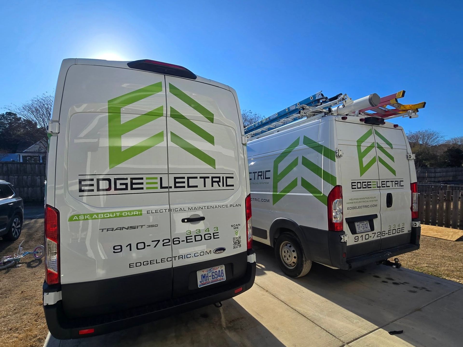 Two white vans with green Edge Electric logos parked outside on a sunny day.
