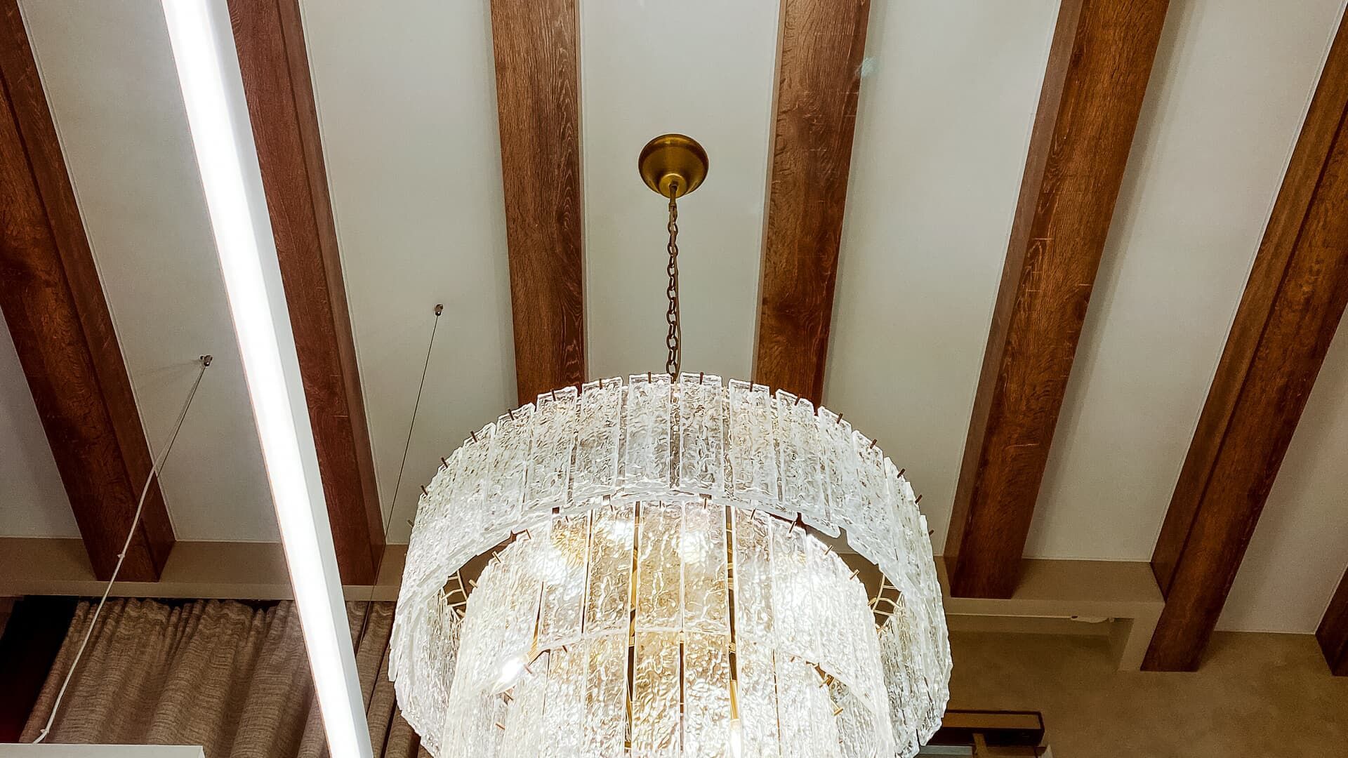 A gold chandelier hangs from a white ceiling with wood beams.