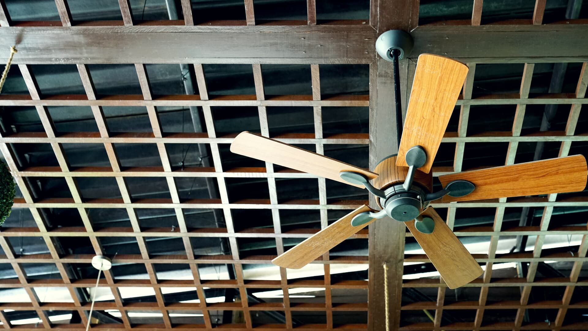 Ceiling fan with wooden blades, hanging below a wooden lattice ceiling.