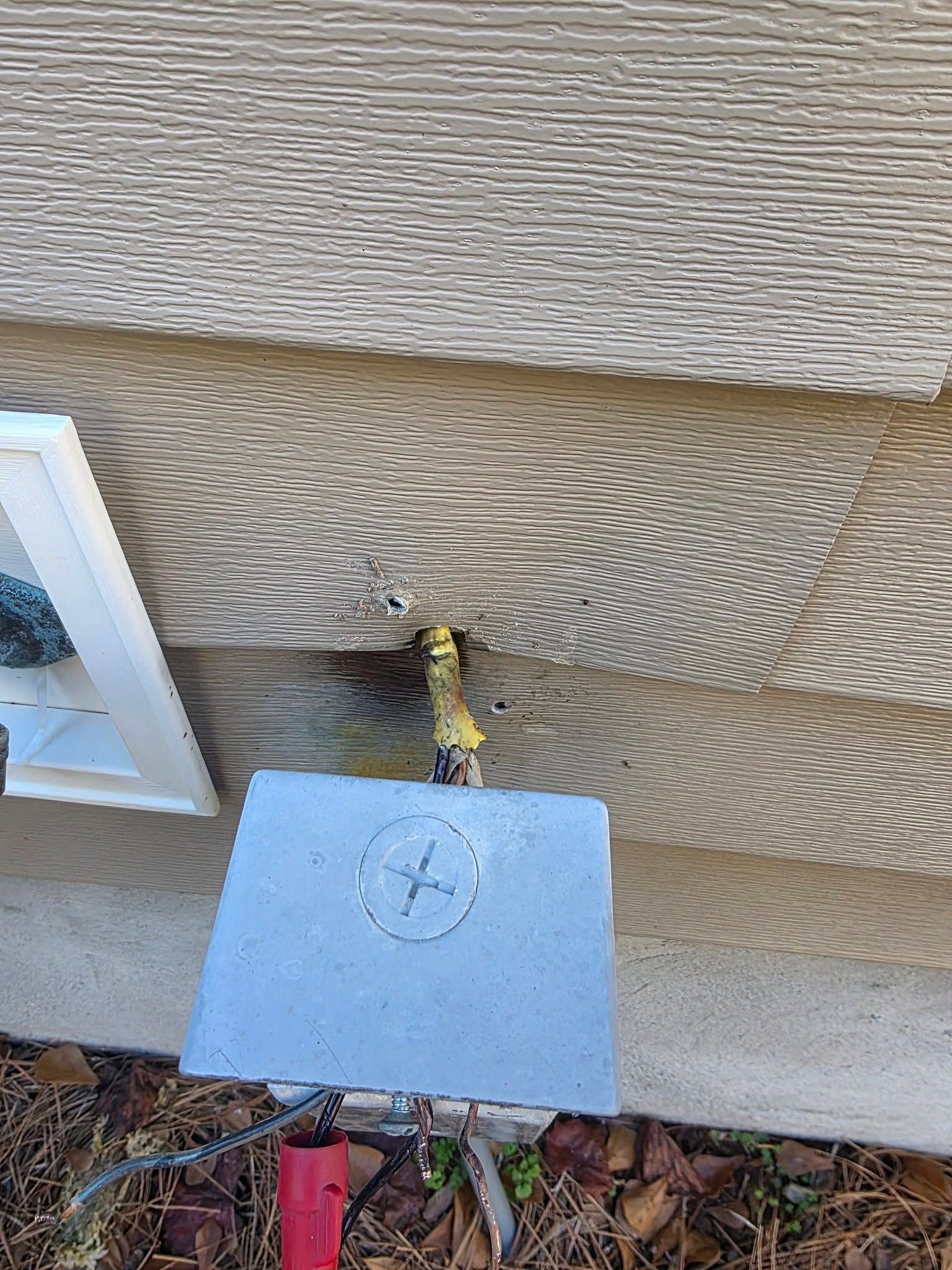 Exterior water spigot with gray concrete pad against gray siding.