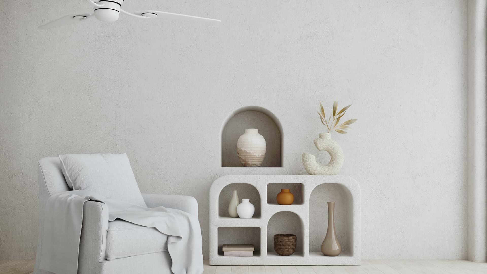 White-walled room with an armchair, arched shelves with decorative vases, and a ceiling fan.