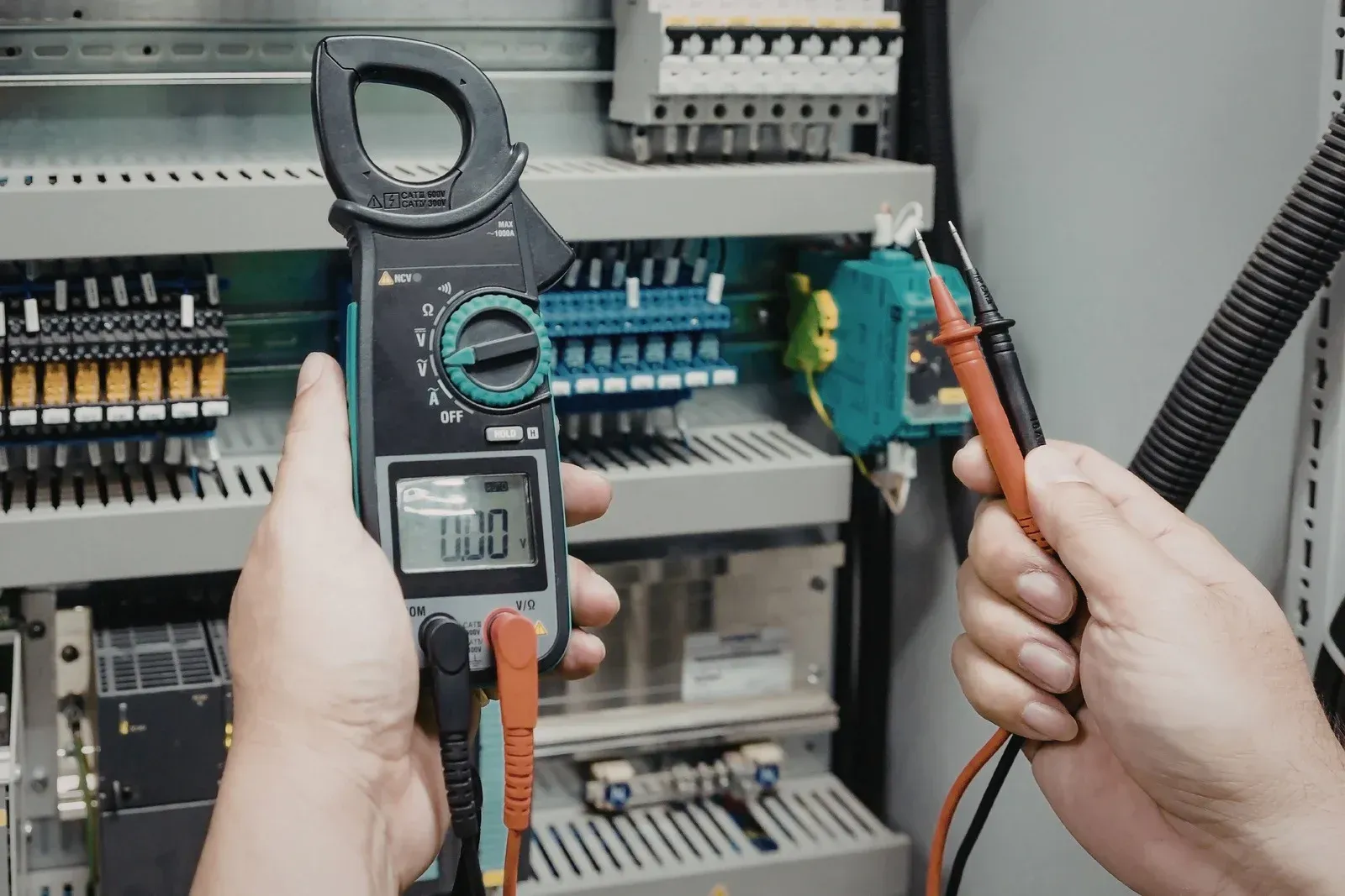 Electrician using a clamp meter to test electrical circuits in a control panel.