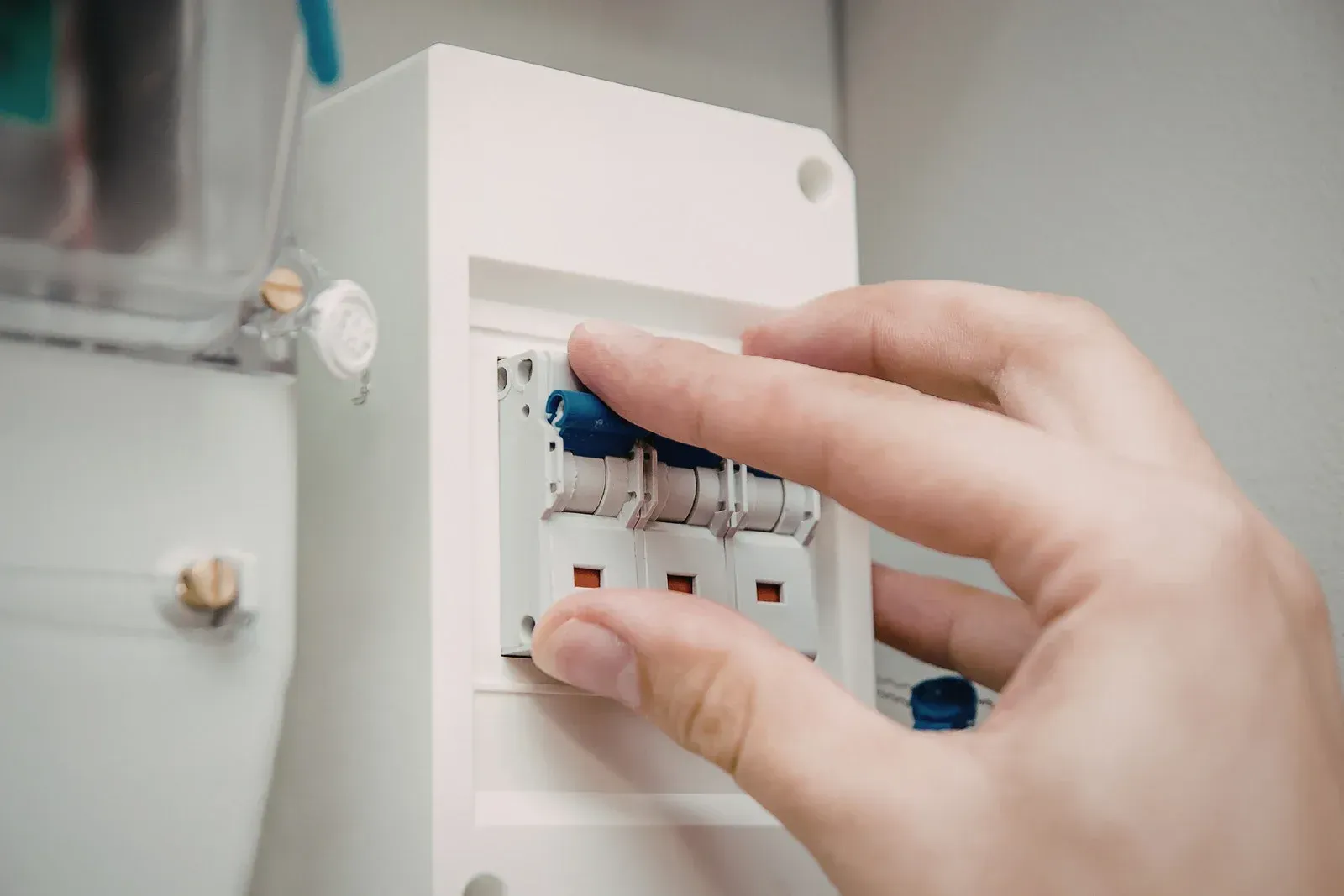 Hand flipping a blue circuit breaker switch in a white electrical panel.