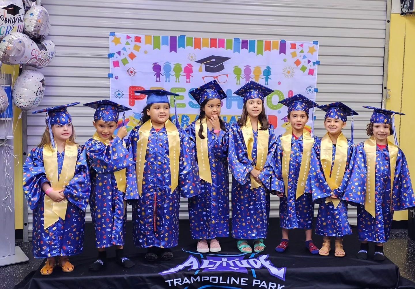 A group of children wearing graduation caps and gowns are posing for a picture.