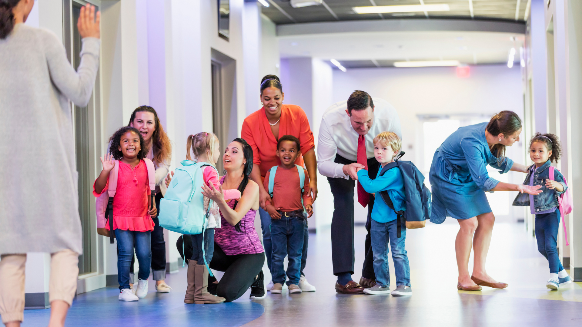 Parents escorting young children into a school hallway.