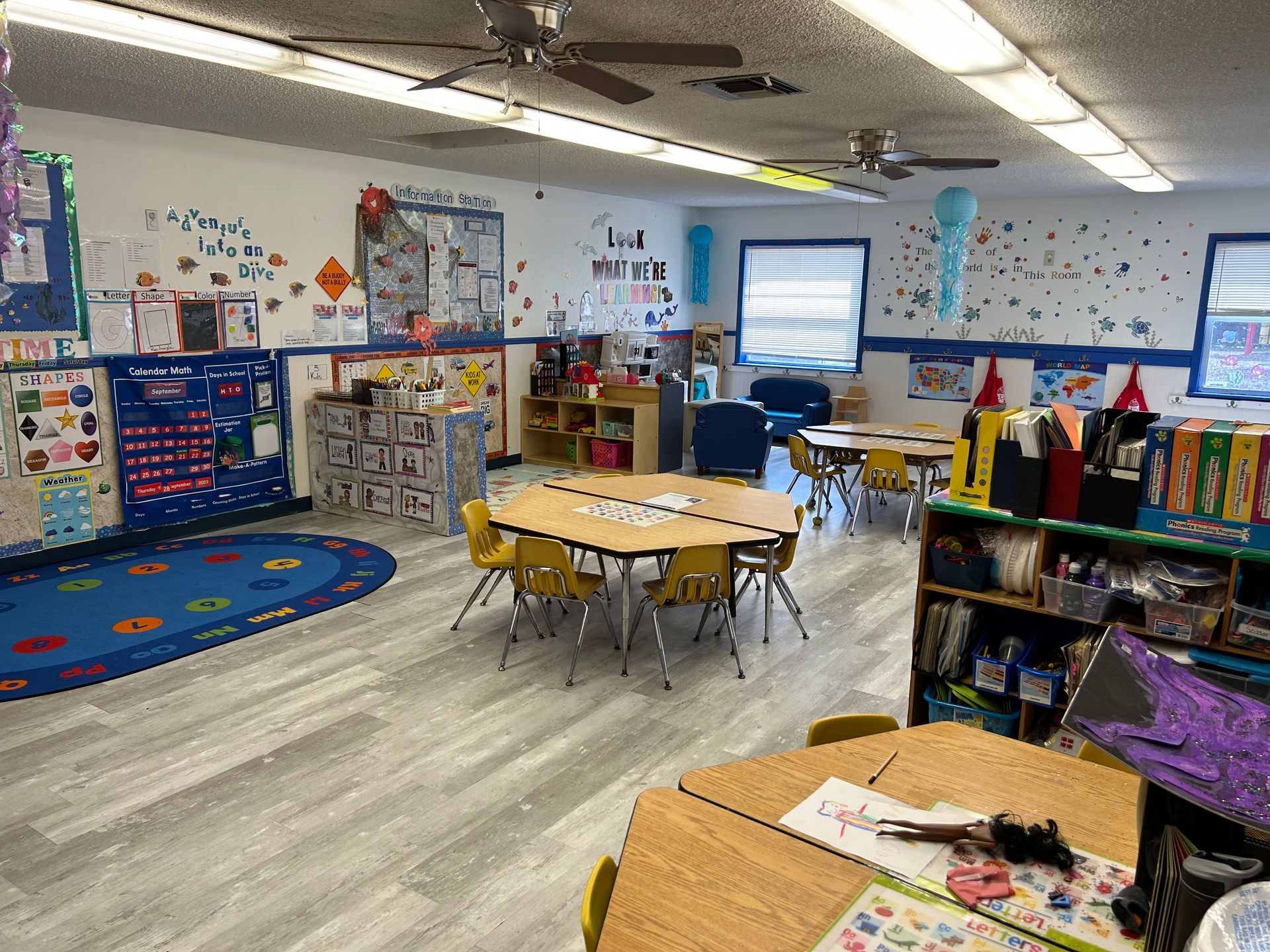 A classroom with tables and chairs and a blue rug.
