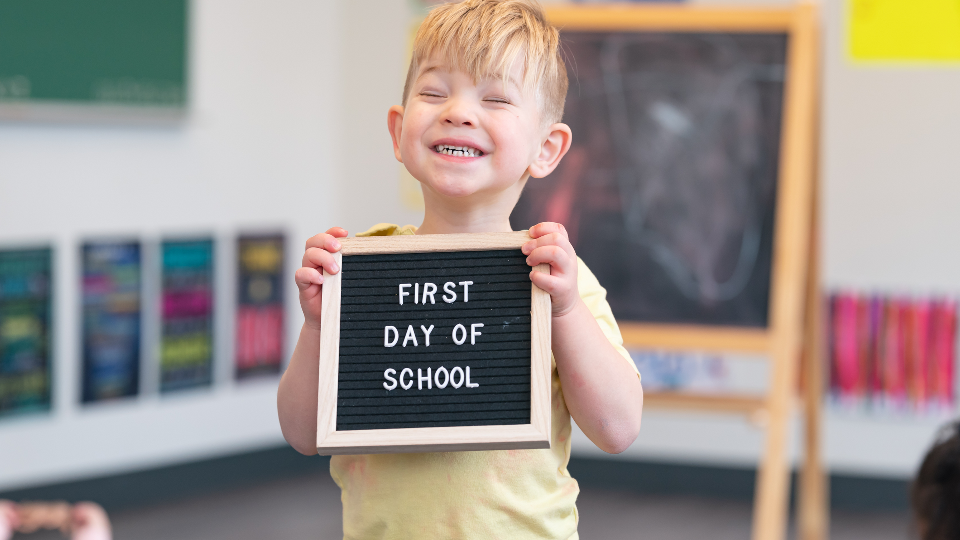 Young child smiles holding a sign that reads 