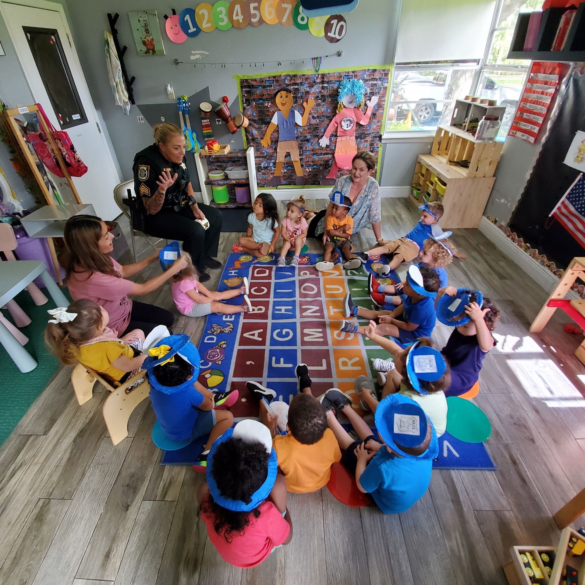 A group of children are sitting in a circle on a rug with the alphabet on it