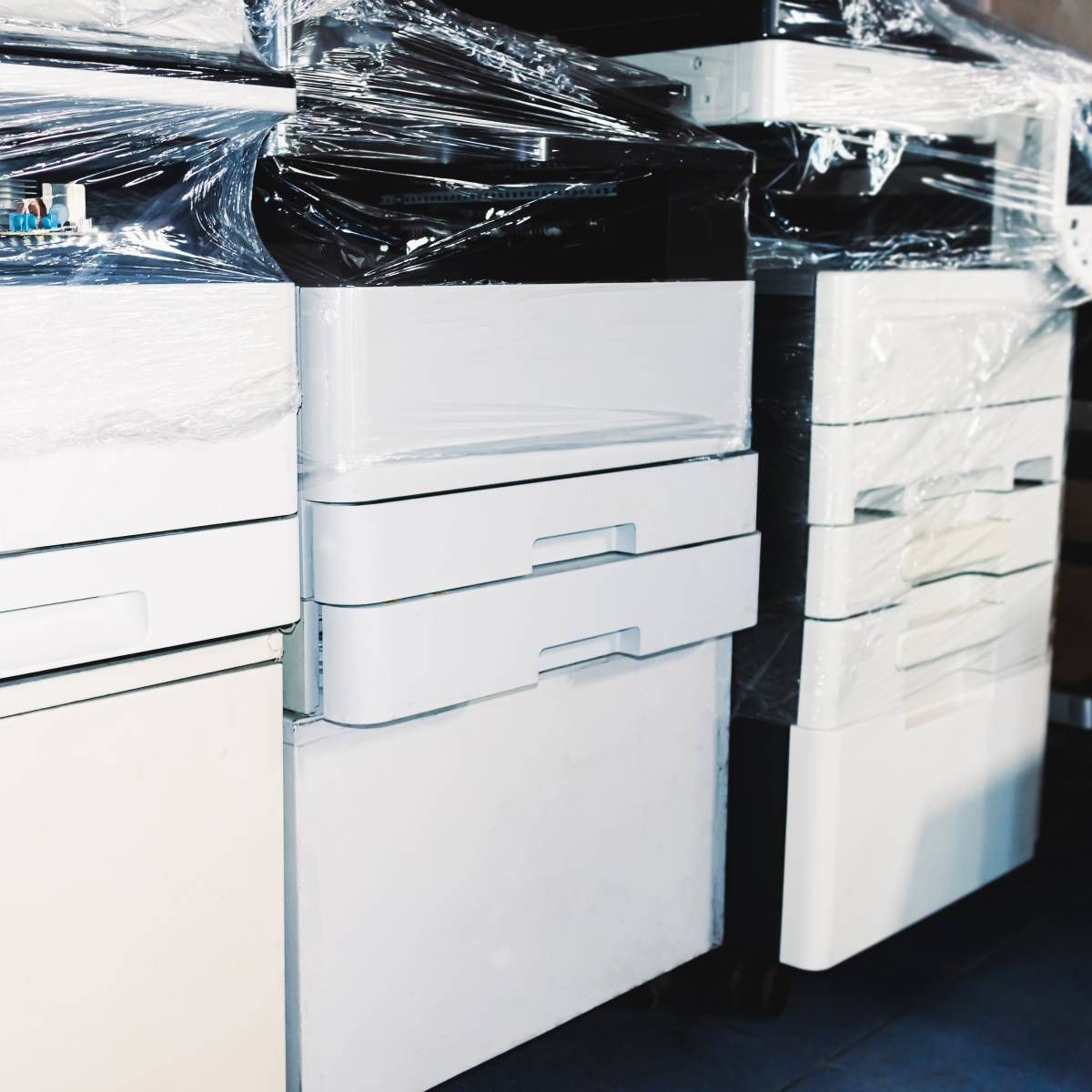 A row of printers are wrapped in plastic and sitting on top of each other.