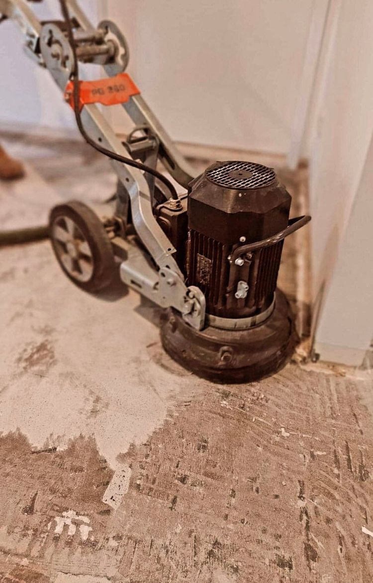 Floor grinder smoothing a concrete floor in a room with a white doorframe.