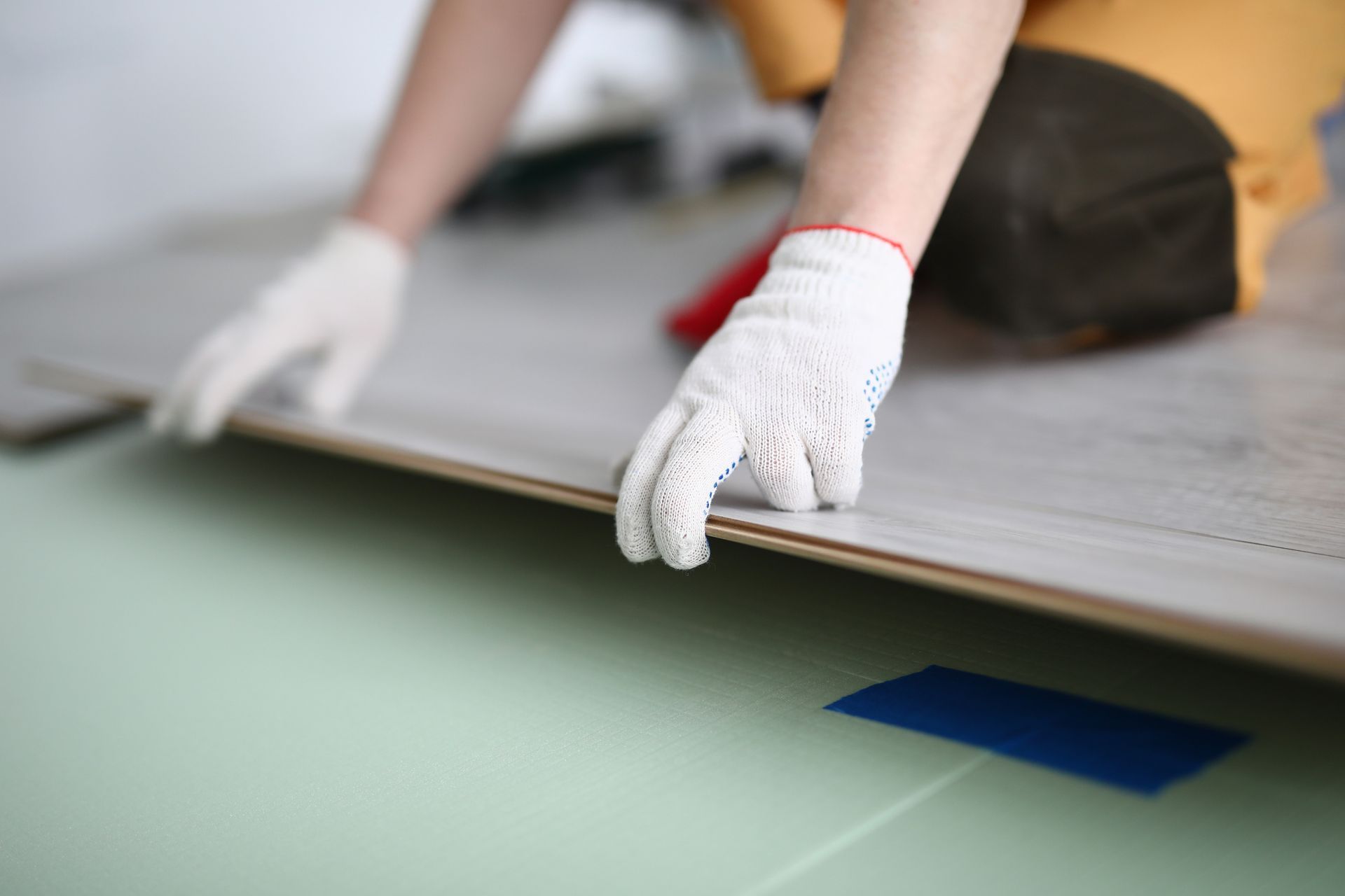 Gloved hands placing a plank during precise floating floor installation over underlayment.