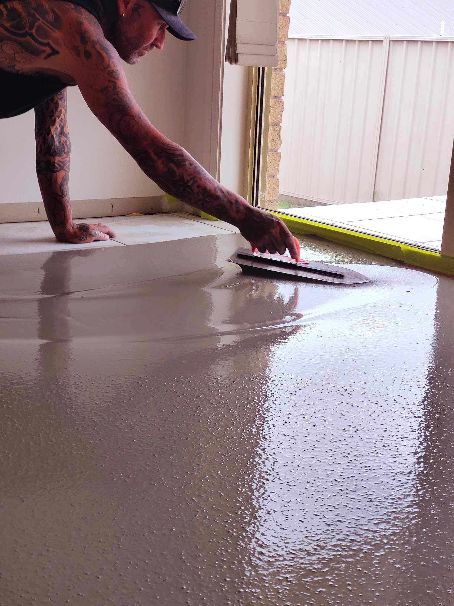 Man smoothing wet concrete floor with a trowel, doorway in background.