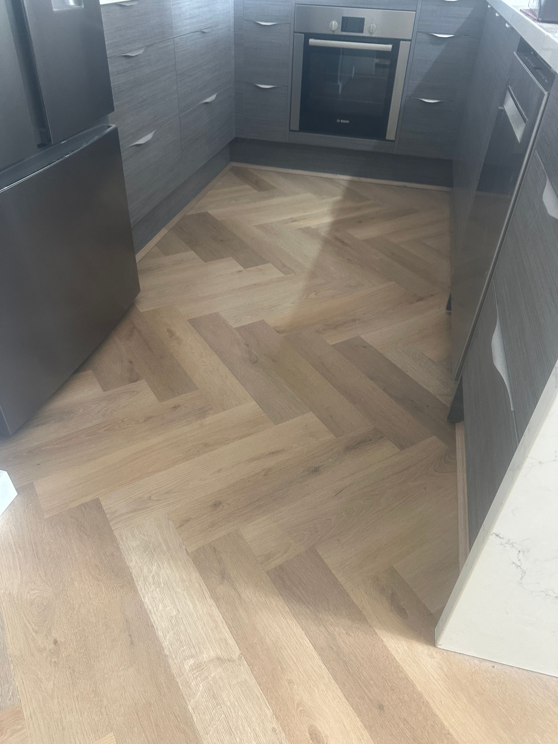 A kitchen with a wooden floor and a herringbone pattern.