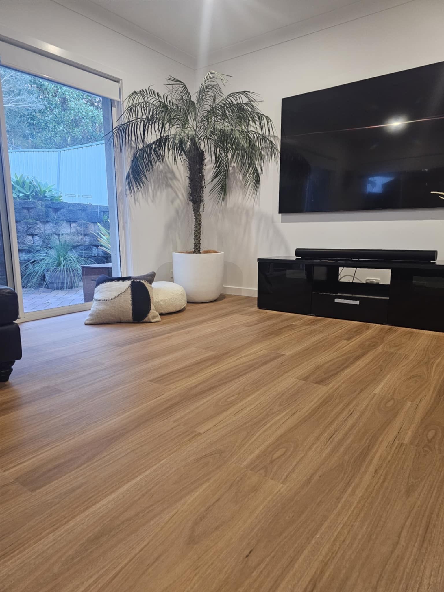 Living room with hardwood floors, large TV, potted plant, and sliding door to a backyard.