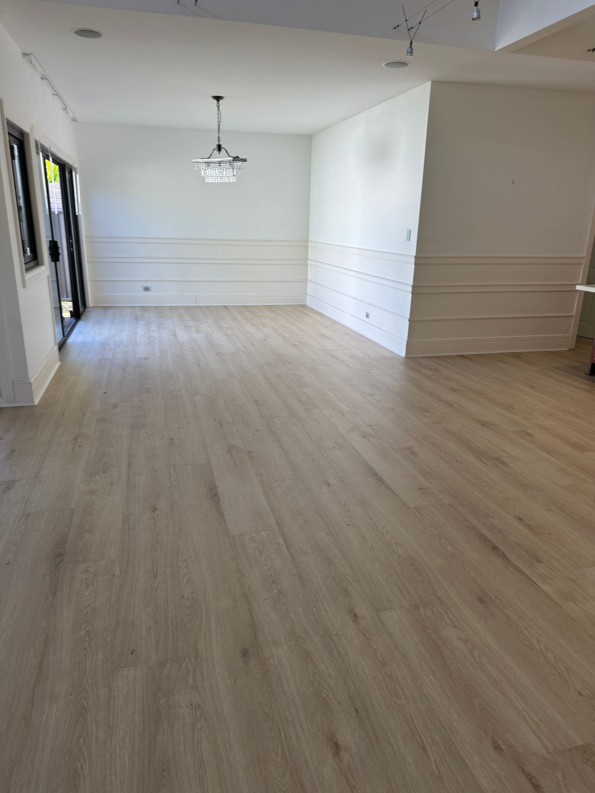 Empty room with light wood floors, white walls, and a chandelier.