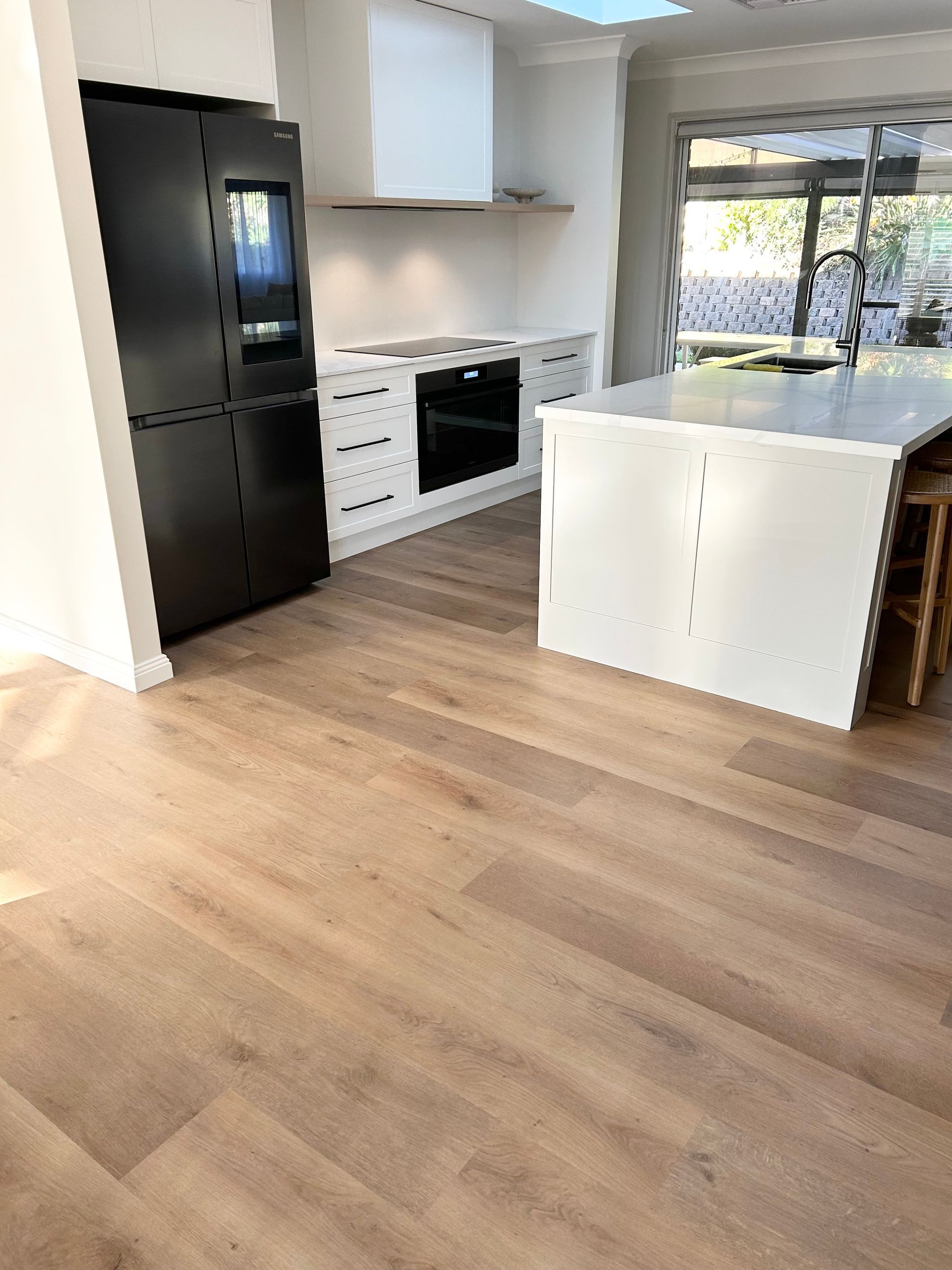 A kitchen with hardwood floors , black appliances , and a large island.