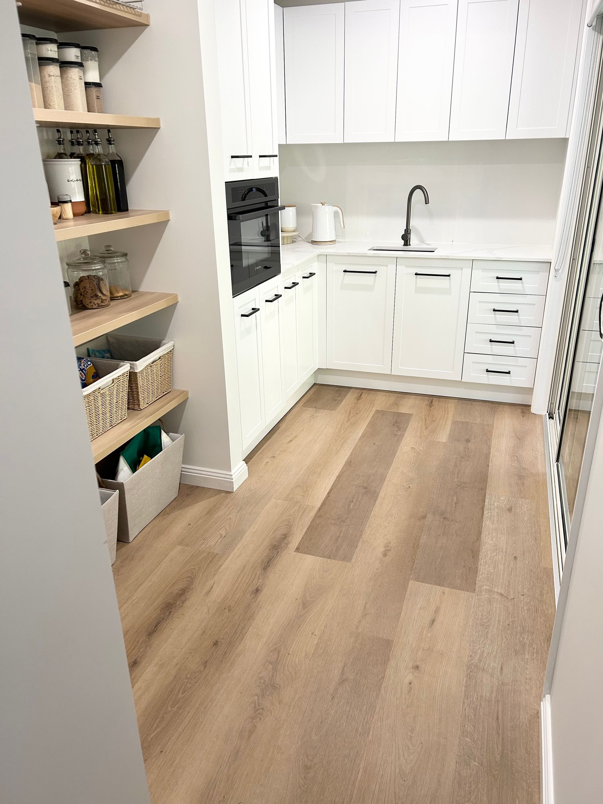A kitchen with white cabinets and wooden floors.