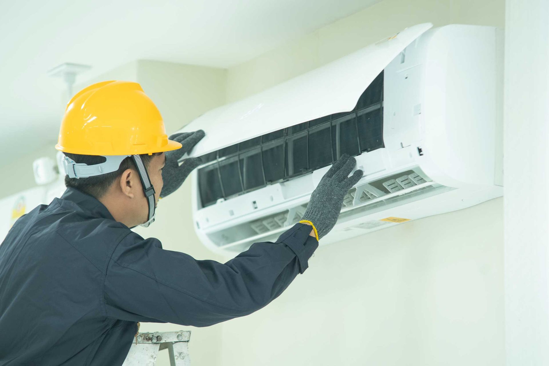 Technician in a yellow hard hat and gloves performing a professional AC installation on a wall unit. Technician in a yellow hard hat and gloves performing a professional AC installation on a wall unit.