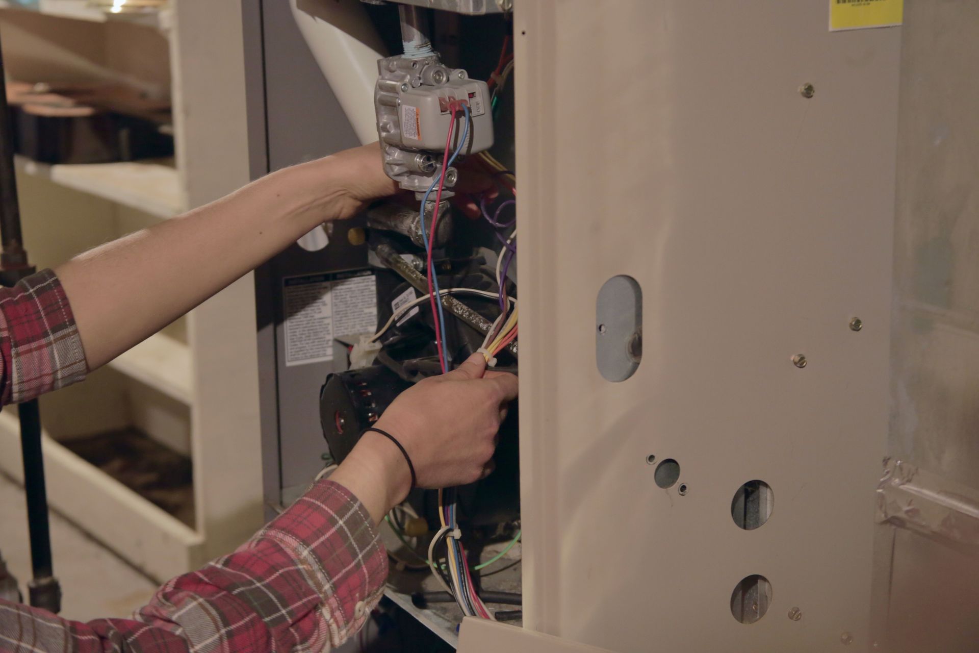A worker is repairing a furnace, focusing on the wiring and components.