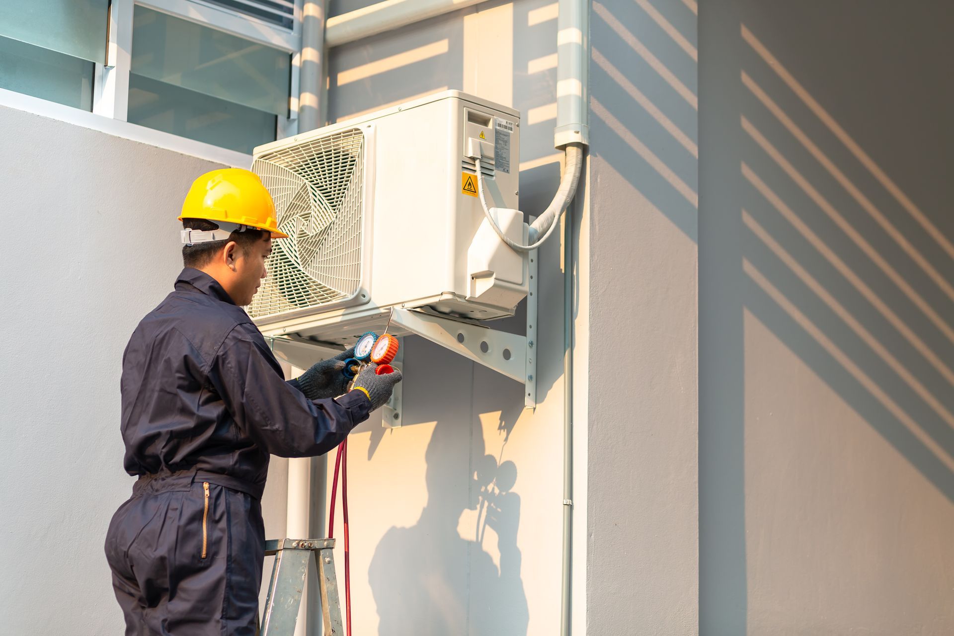 Technician in safety gear checking an outdoor air conditioning unit with pressure gauges.