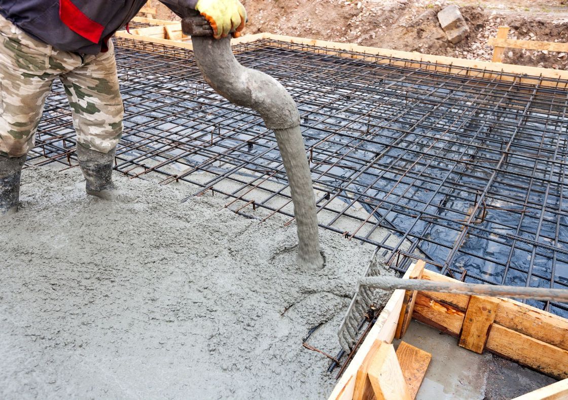 A picture of a worker pouring concrete into concrete slab framework that is reinforced with rebar