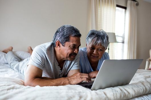 Senior couple lying on bed and using laptop