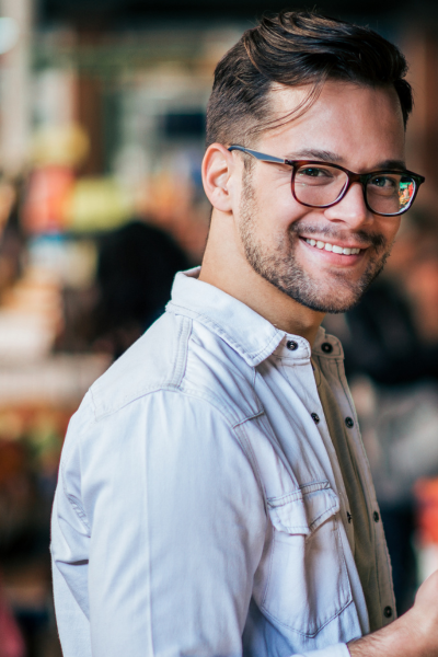 A man wearing glasses and a white shirt is smiling and looking at the camera.