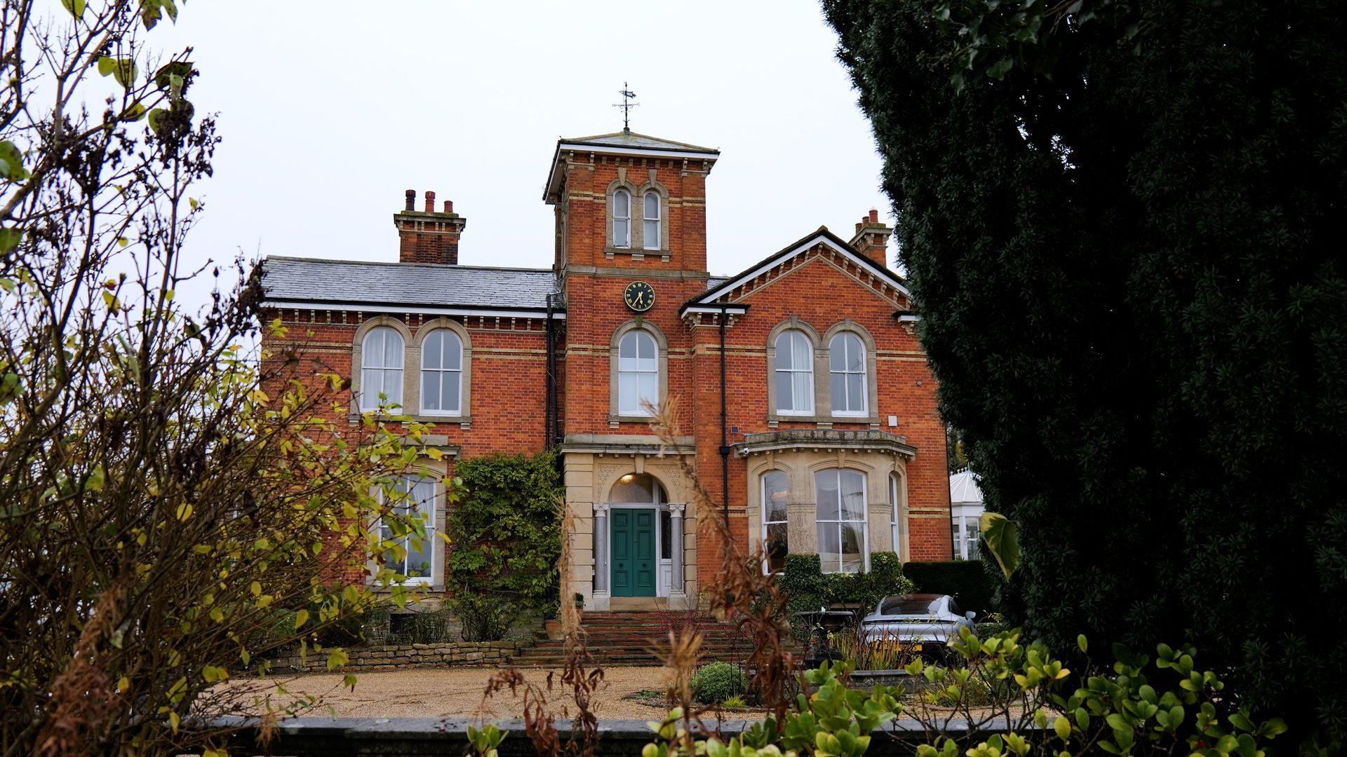 A large brick house with a green door is surrounded by trees and bushes.