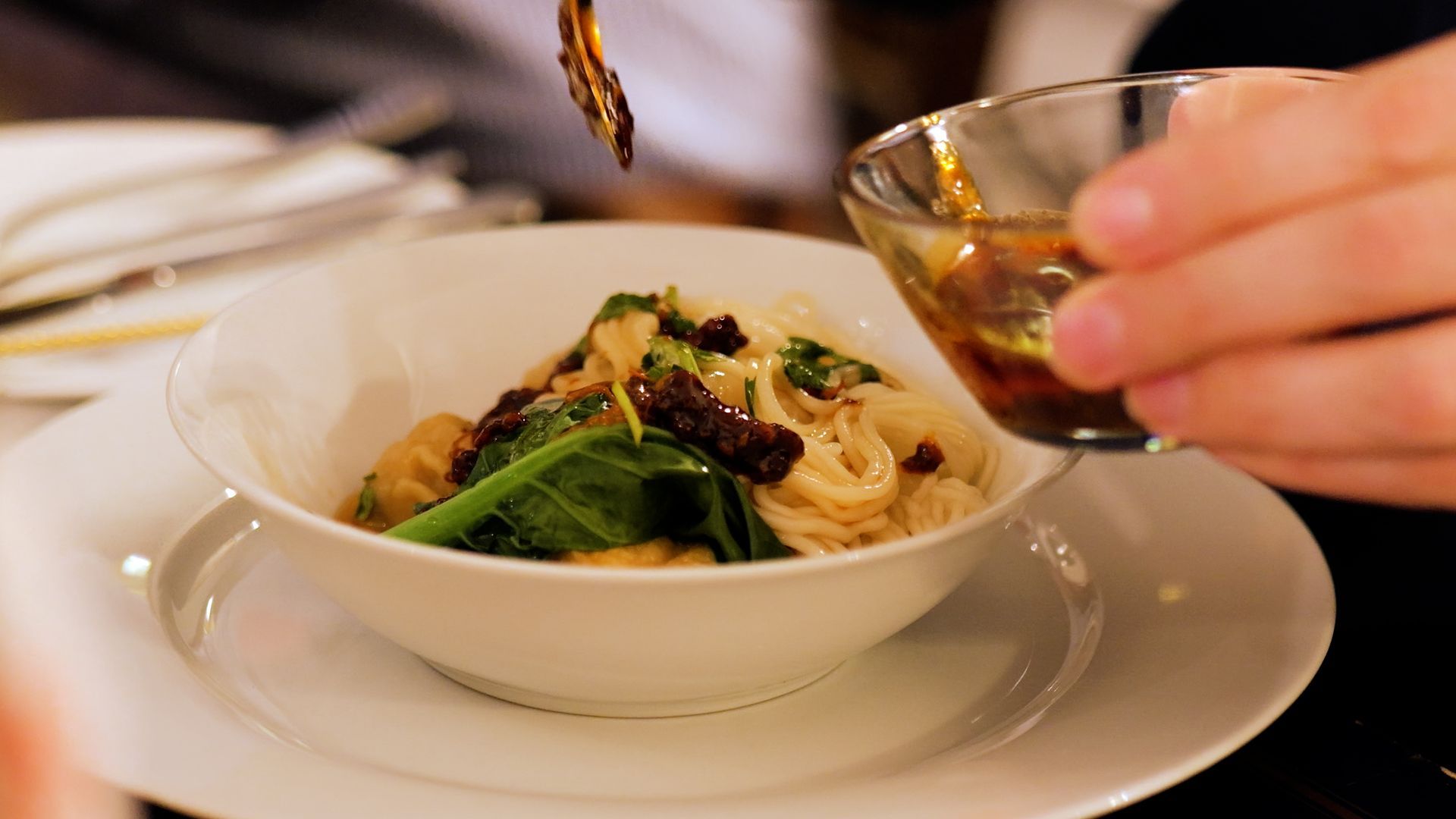 A person is pouring sauce into a bowl of pasta.