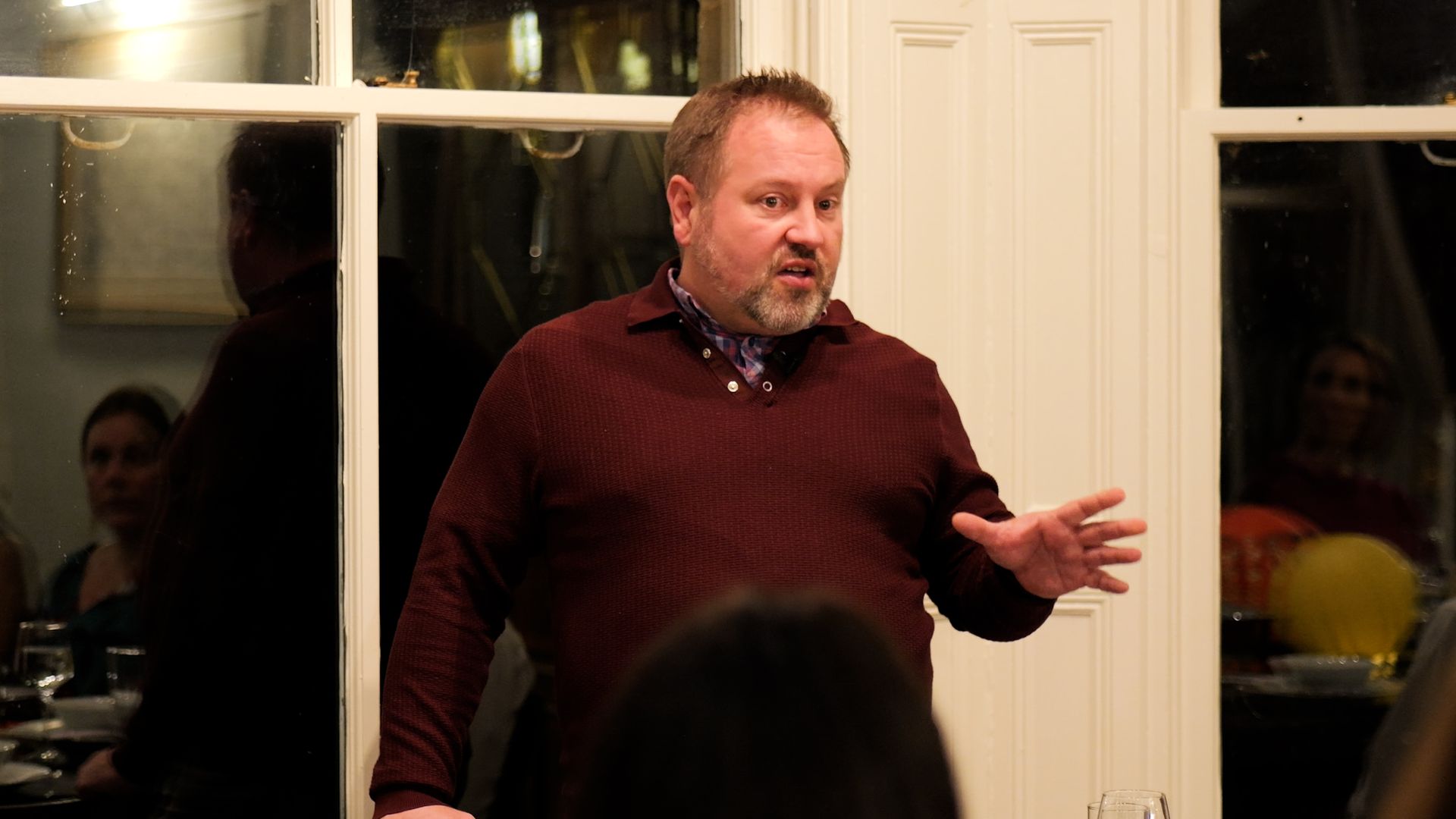 A man in a red sweater is standing in front of a group of people.