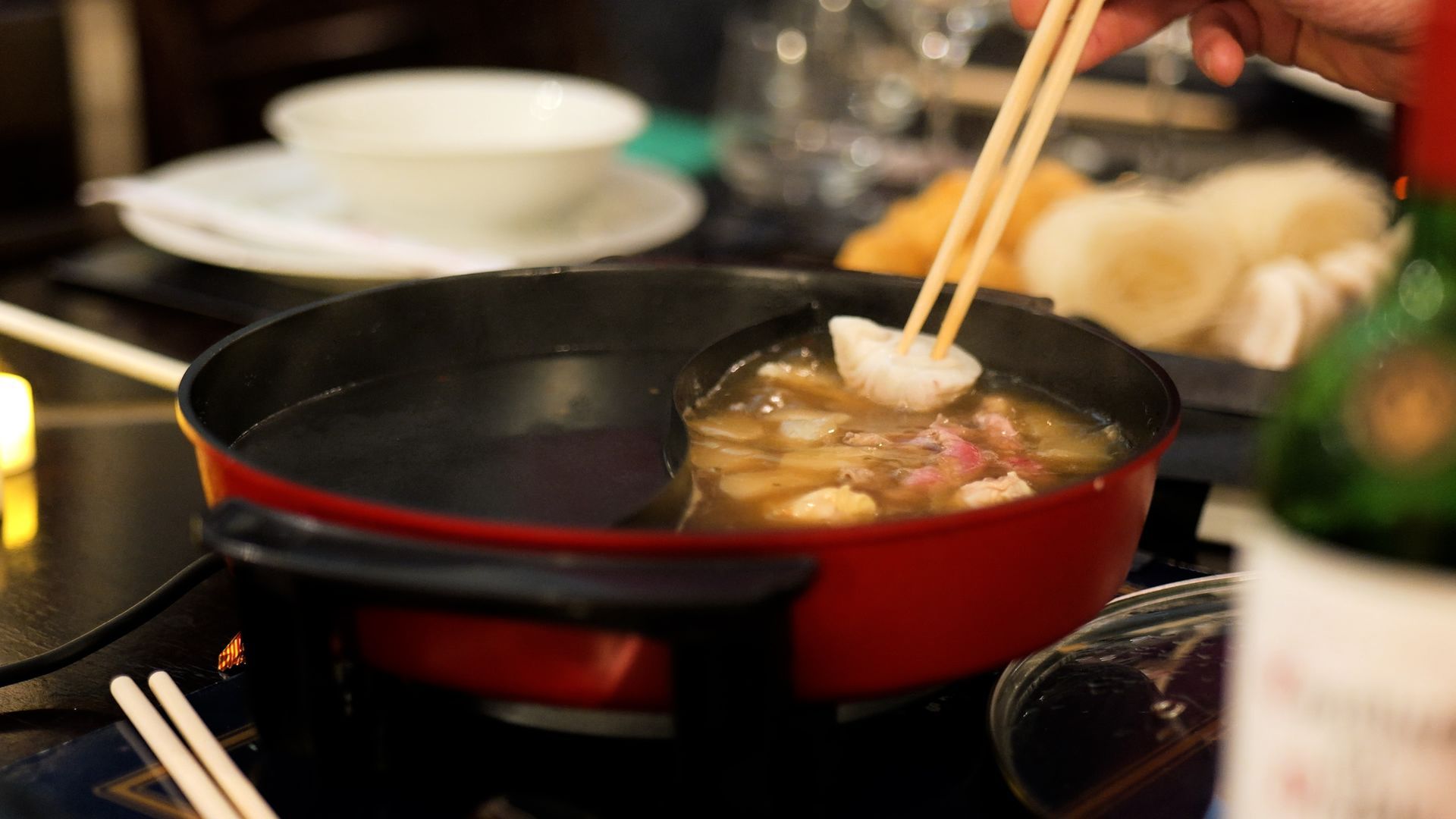 A person is holding chopsticks over a pot of food.