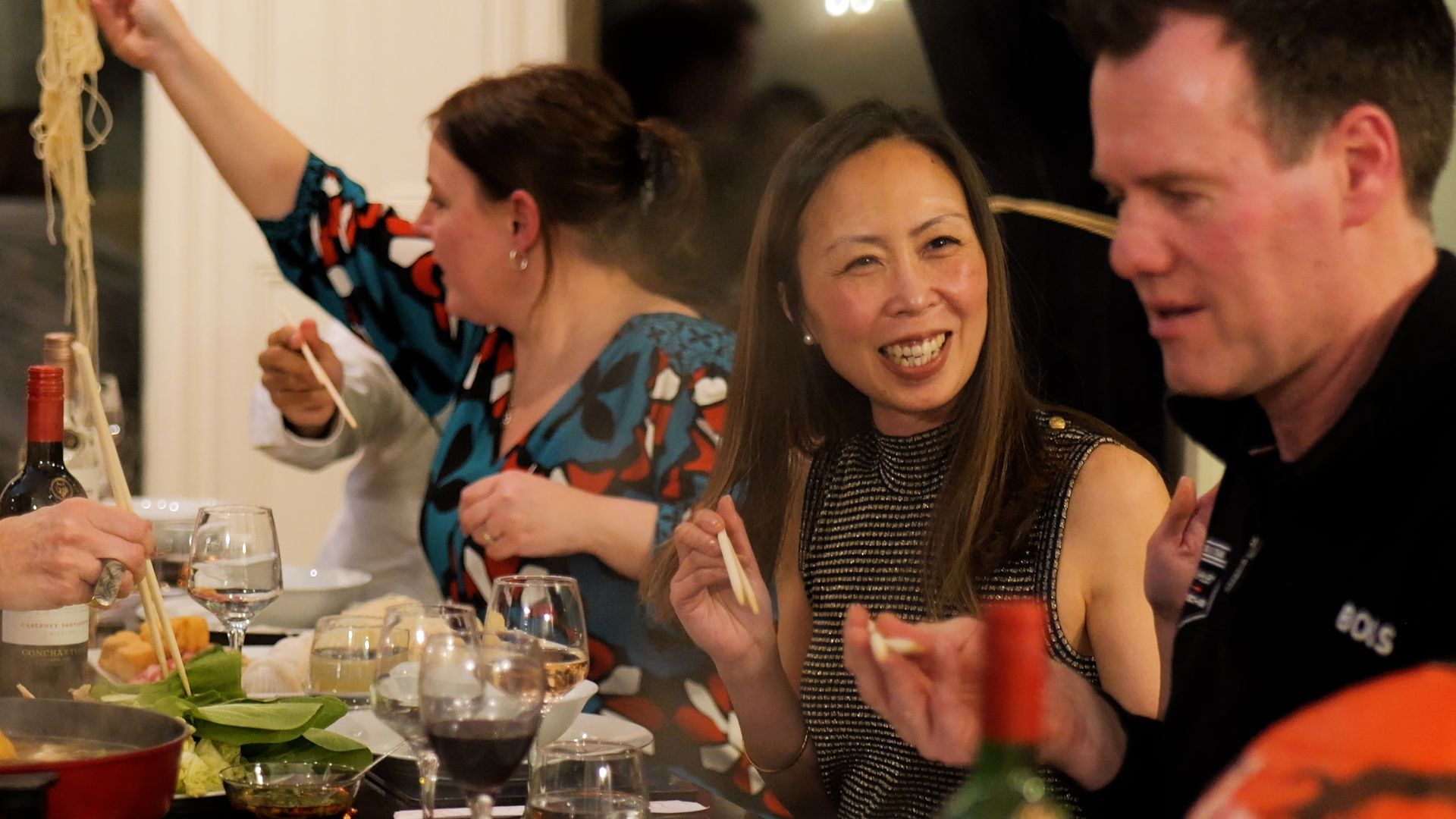 A group of people are sitting at a table eating food and drinking wine.