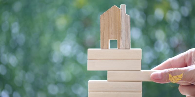 A person is holding a stack of wooden blocks with a house on top of them.