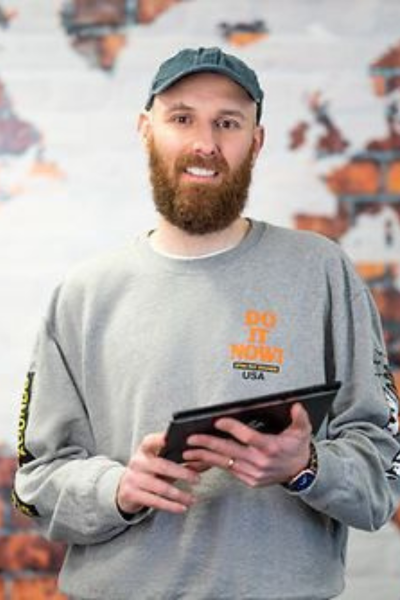 A man with a beard is holding a tablet in front of a map of the world. Richard Nicholls.