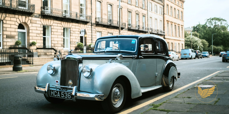 An old car is parked on the side of the road in front of a building.